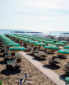 Spiaggia affollata con file di ombrelloni verdi e gialli lungo la costa.