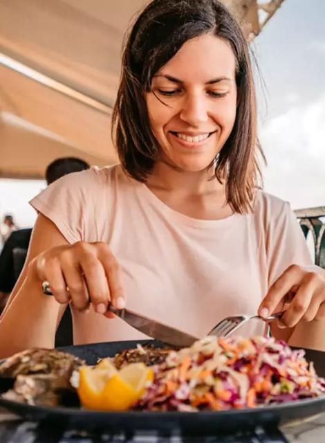 Donna sorridente mentre mangia un piatto colorato di verdure e limone.