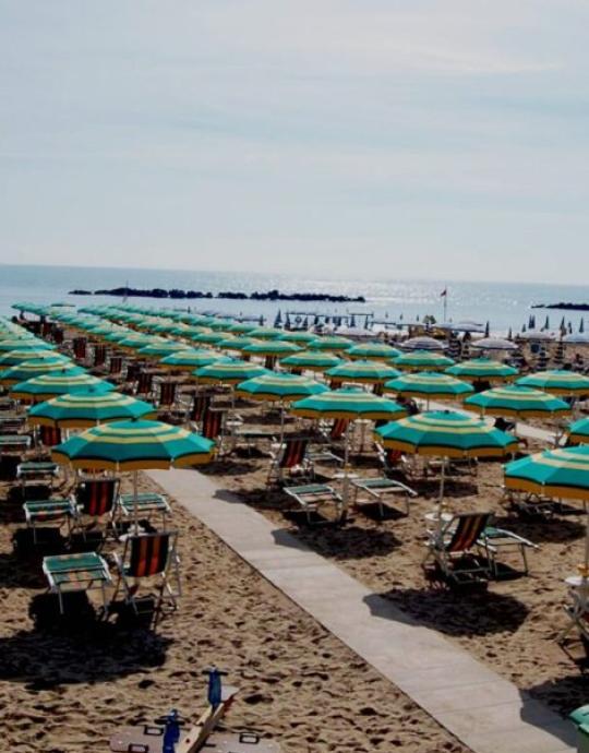 Spiaggia con ombrelloni verdi e gialli, lettini allineati sul bagnasciuga.