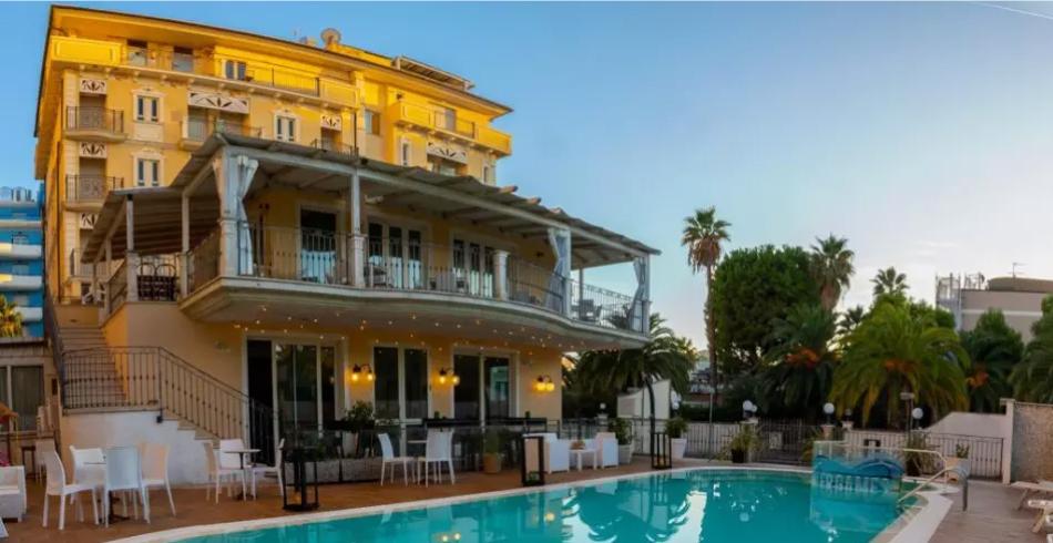 Elegante hotel con piscina, terrazza e palme, ideale per un soggiorno rilassante.